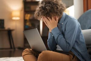 imagem de uma pessoa sentada em frente ao notebook com expressão de chateação e desapontamento pelos erros de SEO em sites